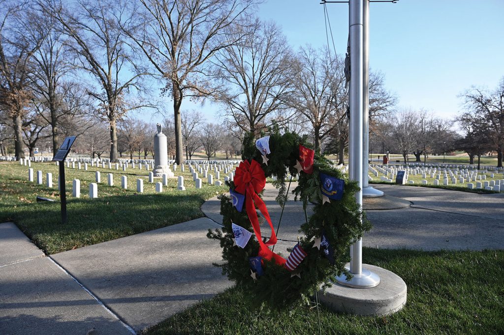 A ceremonial wreath placed at the base of the flagpole at the Fort Leavenworth National Cemetery during Wreaths Across America Day, Dec. 19, 2020. The tall monument with the eagle atop it in the background is the grave of Col. Henry Leavenworth who established “Cantonement Leavenworth” on May 8, 1827.