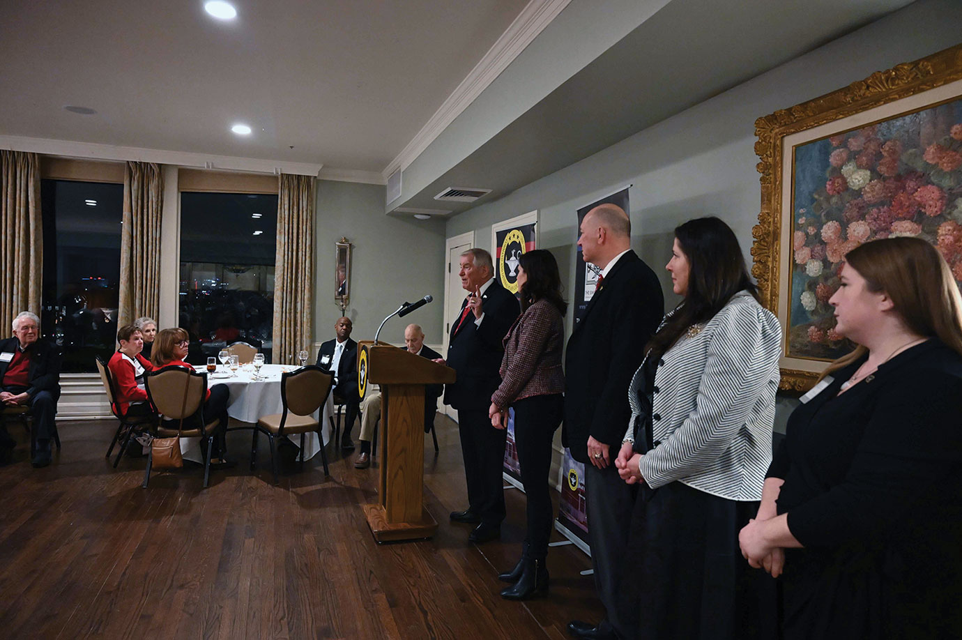 Col. (Ret.) Bob Ulin brings forward the Foundation team that worked with him to administer the Arter-Rowland National Security Forum to thank them publicly during his remarks at the ARNSF holiday social event on Dec. 9, 2025. Ulin is stepping down as the leader of the Forum. From left: Ulin (at podium), Foundation President/CEO Lora Morgan, Simons Center Senior Research Fellow John Nelson, Foundation Director of Operations Stephenie Cole, and Foundation Assistant Operations Officer Elizabeth Hill.